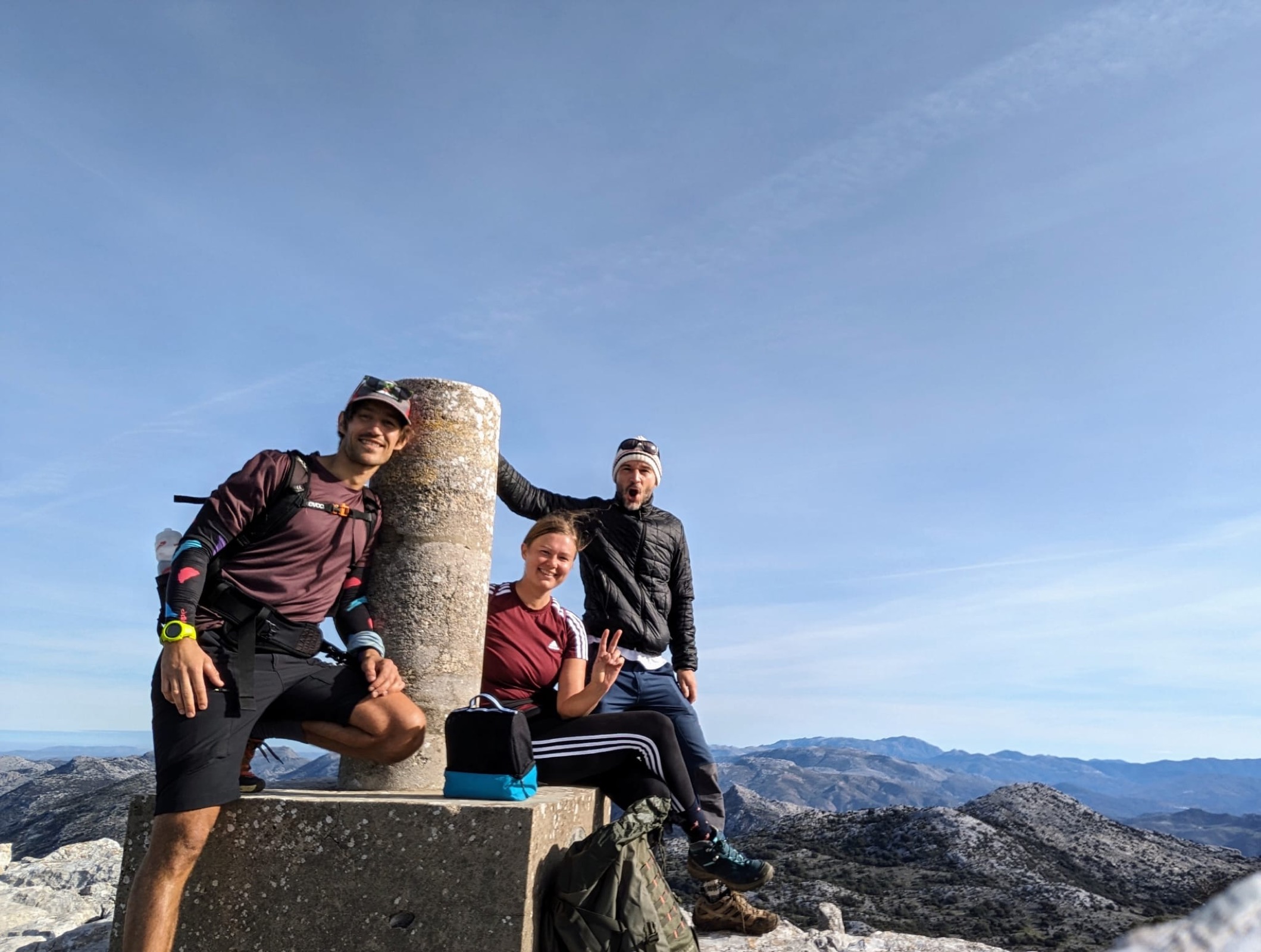Three friends at a summit trig point in the Sierra de Grazalema