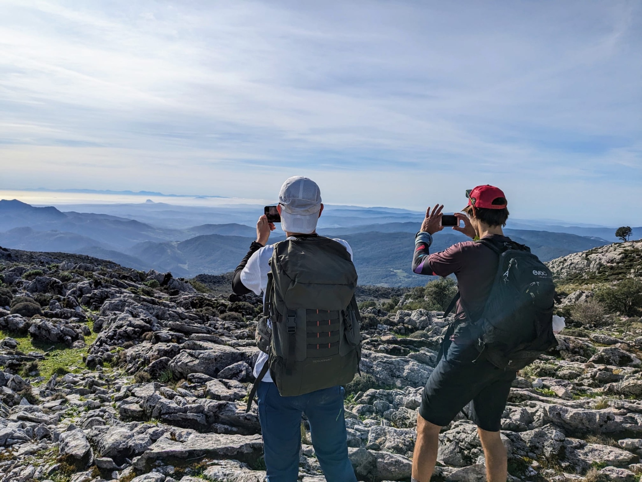 Two hikers photographing the view from a limestone ridge near Cortes